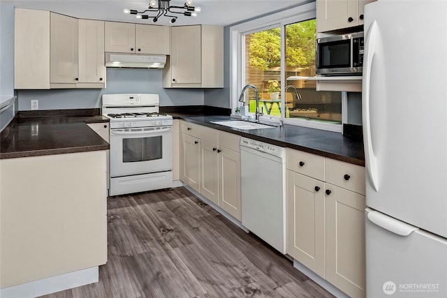kitchen with a sink, dark countertops, under cabinet range hood, and white appliances