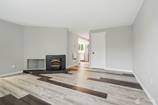 unfurnished living room featuring baseboards, a wood stove, and wood finished floors