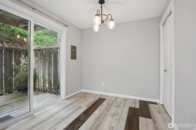 unfurnished dining area with an inviting chandelier, baseboards, wood finished floors, and electric panel