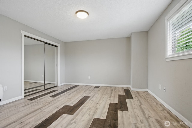 unfurnished bedroom featuring a closet, a textured ceiling, baseboards, and wood finished floors