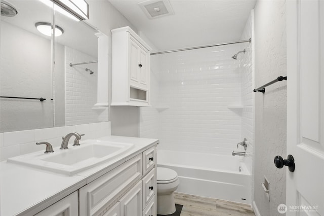 bathroom with vanity, toilet, wood finished floors, shower / bathing tub combination, and visible vents