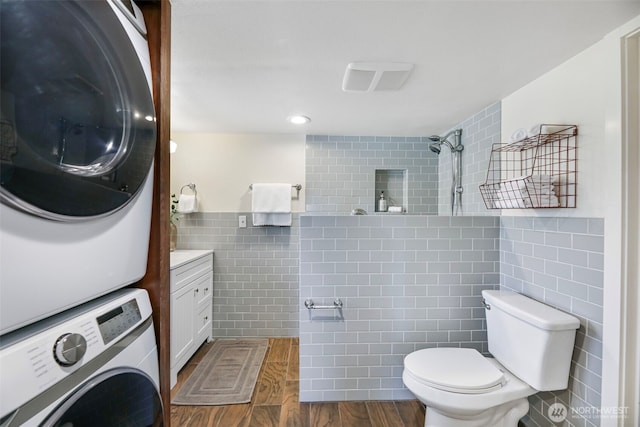 full bathroom featuring tile walls, stacked washer and clothes dryer, toilet, vanity, and tiled shower