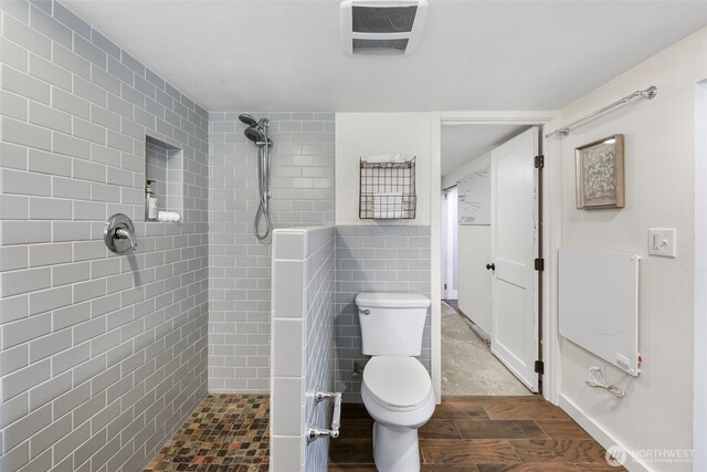 full bathroom featuring toilet, tiled shower, tile walls, and wood finished floors