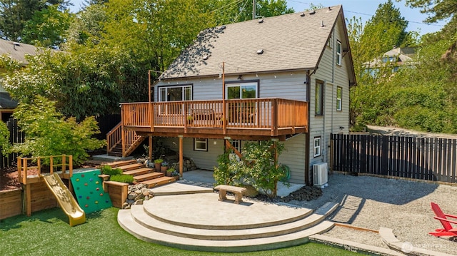 rear view of house with a patio area, a wooden deck, central AC unit, roof with shingles, and a playground