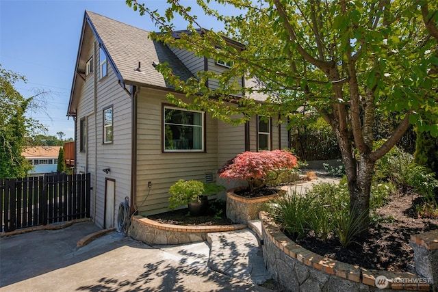 view of side of home with fence, roof with shingles, and a patio area