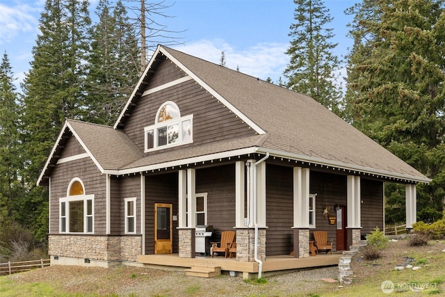 view of front of property with stone siding, a porch, a shingled roof, and fence