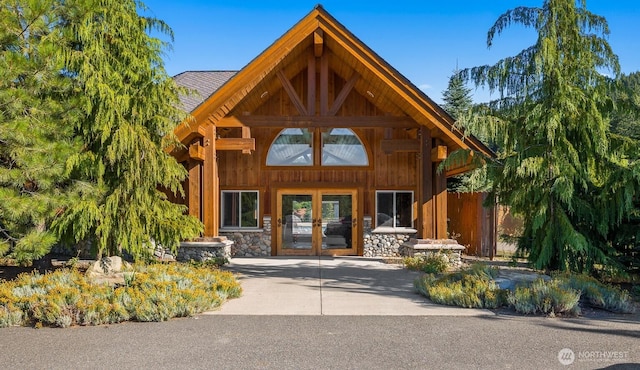 doorway to property with stone siding, french doors, and fence