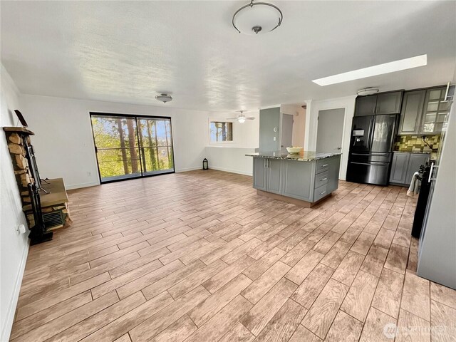 unfurnished living room with a skylight, baseboards, ceiling fan, and light wood-style flooring