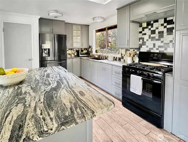 kitchen with a sink, stainless steel fridge with ice dispenser, gray cabinets, black range with gas cooktop, and backsplash