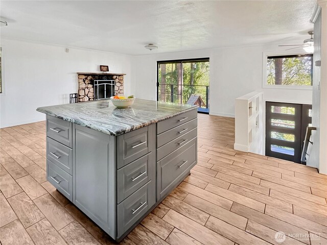 kitchen featuring light stone counters, a stone fireplace, gray cabinets, wood tiled floor, and a kitchen island
