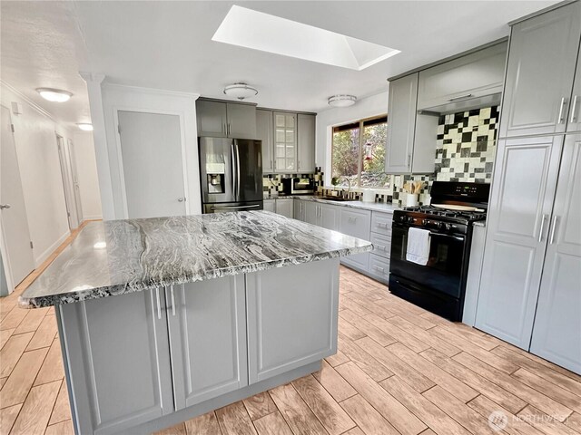 kitchen with gray cabinets, a kitchen island, a skylight, black gas stove, and stainless steel fridge