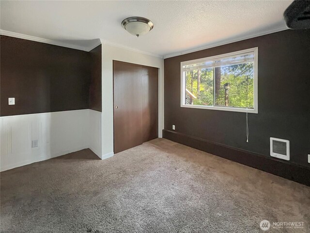 unfurnished bedroom with a textured ceiling, visible vents, carpet floors, a closet, and ornamental molding