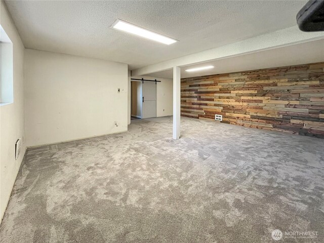 finished basement featuring wooden walls, carpet, a textured ceiling, and visible vents