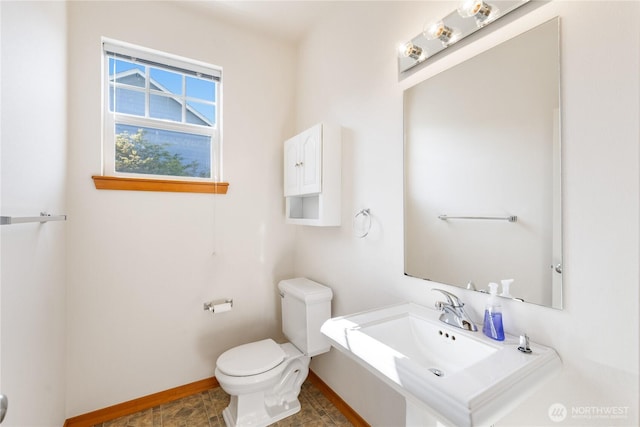 half bath featuring toilet, baseboards, and a sink