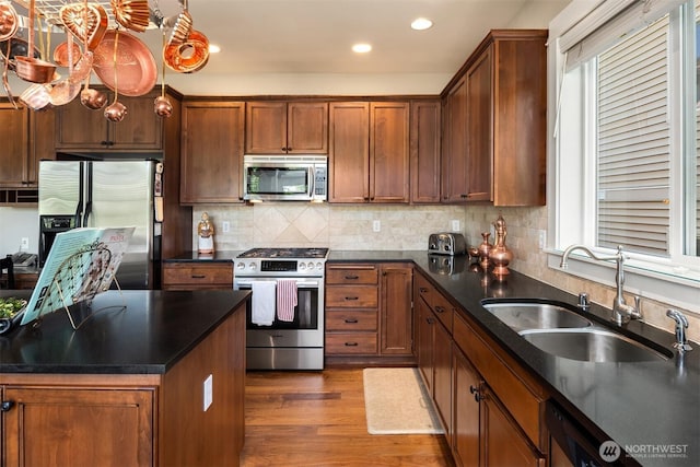 kitchen with dark countertops, wood finished floors, a sink, stainless steel appliances, and recessed lighting