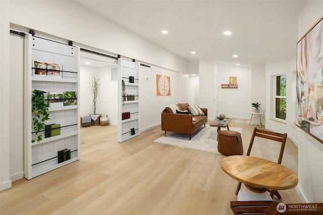 living area with recessed lighting, baseboards, a barn door, and light wood finished floors