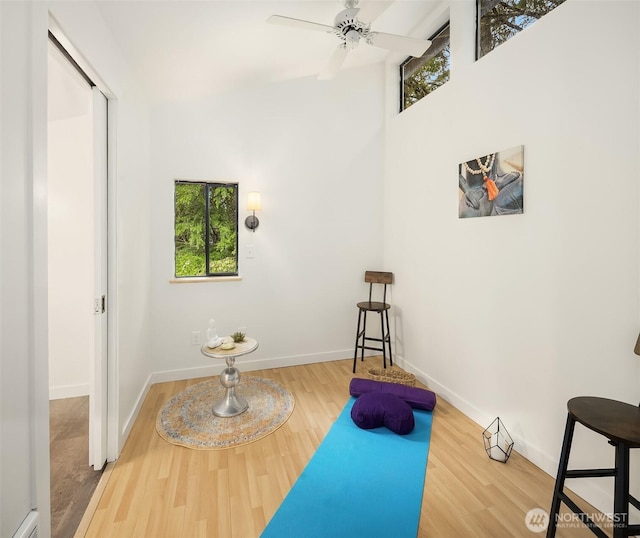 exercise room featuring baseboards, ceiling fan, wood finished floors, and a towering ceiling