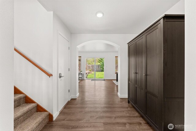 corridor featuring baseboards, arched walkways, wood finished floors, and stairway