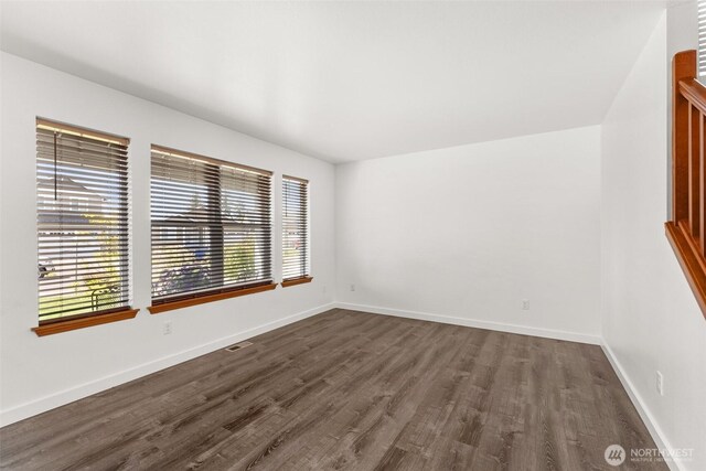 empty room with dark wood-style flooring, baseboards, and visible vents
