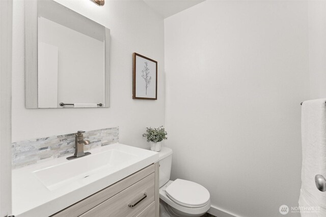 half bathroom with vanity, baseboards, toilet, and tasteful backsplash