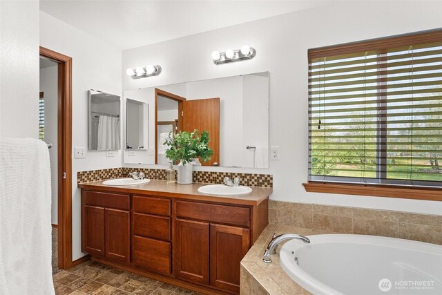 full bathroom with double vanity, a tub with jets, a sink, and tasteful backsplash