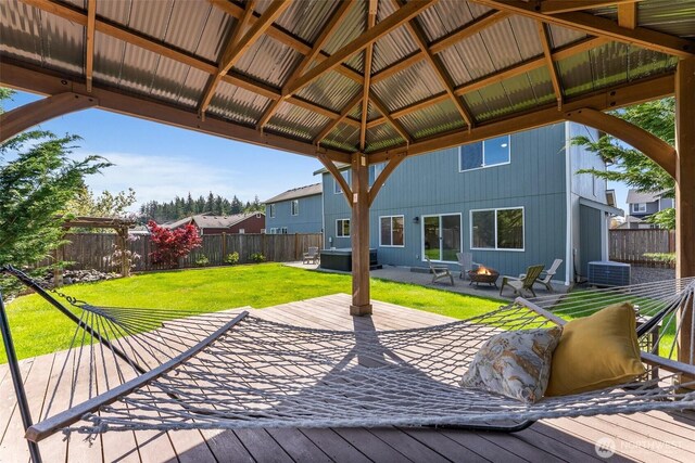 deck with a gazebo, a jacuzzi, a fenced backyard, a yard, and a fire pit