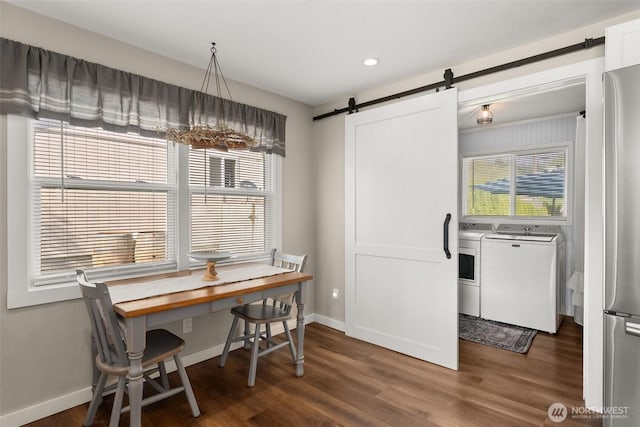 dining room featuring a healthy amount of sunlight, dark wood-type flooring, a barn door, and washing machine and clothes dryer