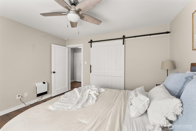 bedroom with heating unit, baseboards, dark wood-type flooring, a barn door, and a ceiling fan