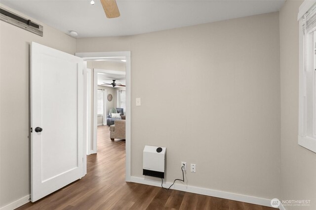 unfurnished bedroom with dark wood-type flooring, heating unit, ceiling fan, and baseboards