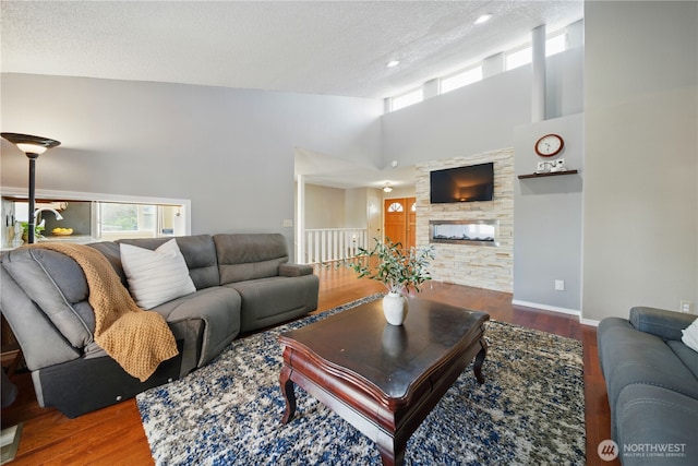 living room with a stone fireplace, a textured ceiling, wood finished floors, high vaulted ceiling, and recessed lighting