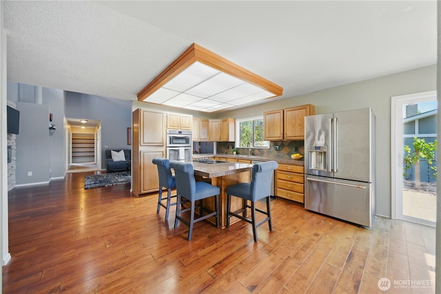 kitchen featuring appliances with stainless steel finishes, a breakfast bar, a sink, light wood finished floors, and a center island