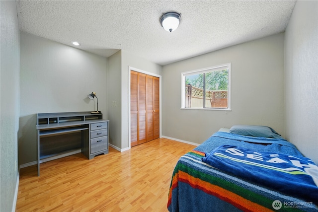 bedroom featuring a textured ceiling, baseboards, a closet, and light wood-style flooring