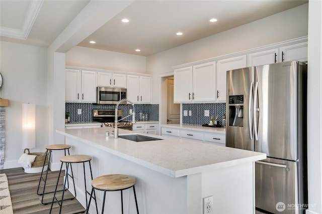 kitchen featuring decorative backsplash, a kitchen island with sink, a kitchen breakfast bar, white cabinets, and appliances with stainless steel finishes