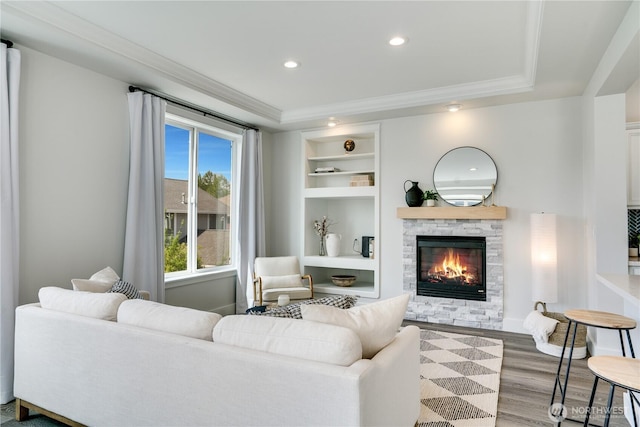 living area with built in features, ornamental molding, a fireplace, and wood finished floors