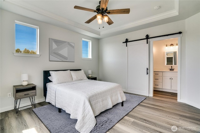 bedroom with crown molding, baseboards, a barn door, a raised ceiling, and light wood-style flooring