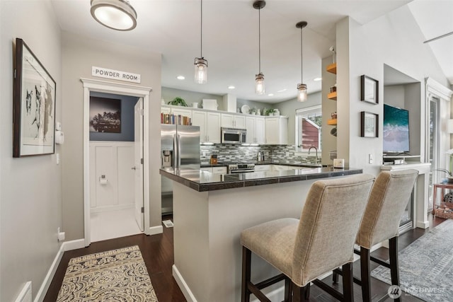 kitchen featuring appliances with stainless steel finishes, white cabinets, dark countertops, dark wood finished floors, and a kitchen breakfast bar