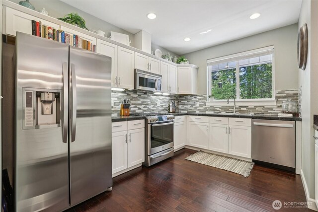 kitchen with stainless steel appliances, dark countertops, a sink, tasteful backsplash, and white cabinetry