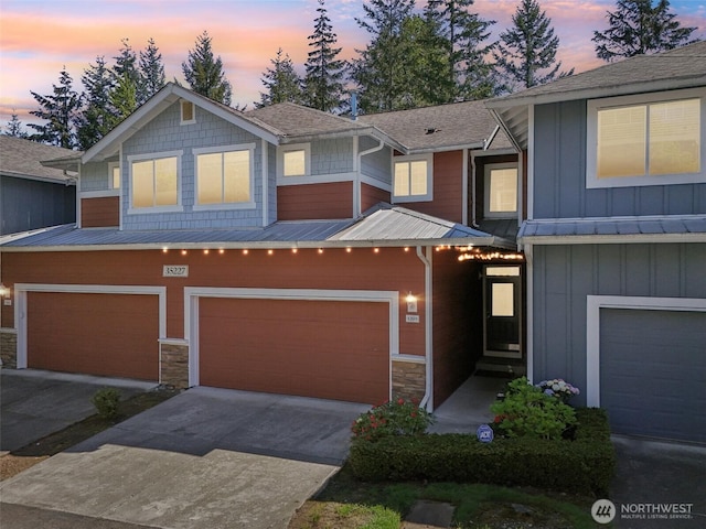 view of property featuring an attached garage, board and batten siding, stone siding, concrete driveway, and metal roof