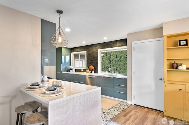 kitchen featuring light countertops, stainless steel dishwasher, light wood-type flooring, and a sink