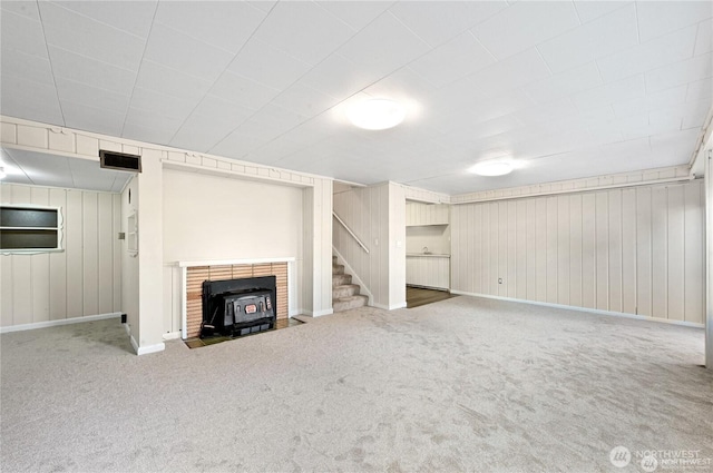 unfurnished living room featuring a wood stove, carpet, stairs, baseboards, and visible vents