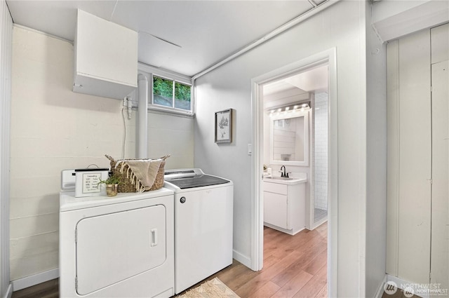 clothes washing area featuring laundry area, baseboards, washing machine and clothes dryer, a sink, and light wood-style flooring