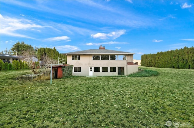 rear view of house with a lawn, a chimney, and stucco siding