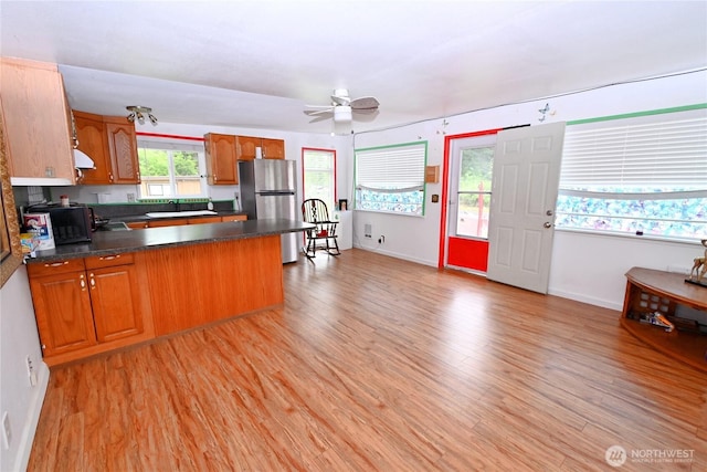 kitchen featuring dark countertops, a sink, light wood-style floors, freestanding refrigerator, and a peninsula