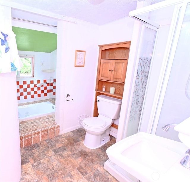bathroom featuring toilet, tiled tub, a sink, stone finish flooring, and a stall shower