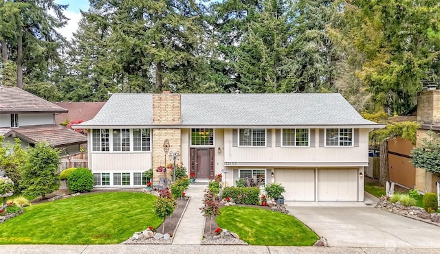split foyer home featuring a garage, a front yard, roof with shingles, a chimney, and concrete driveway