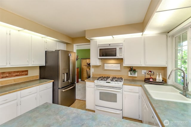 kitchen featuring white appliances, white cabinets, a sink, and light countertops