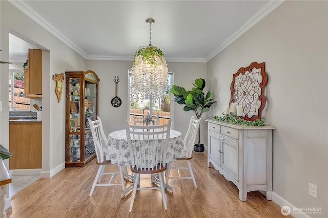 dining space with light wood-type flooring, ornamental molding, healthy amount of natural light, and baseboards