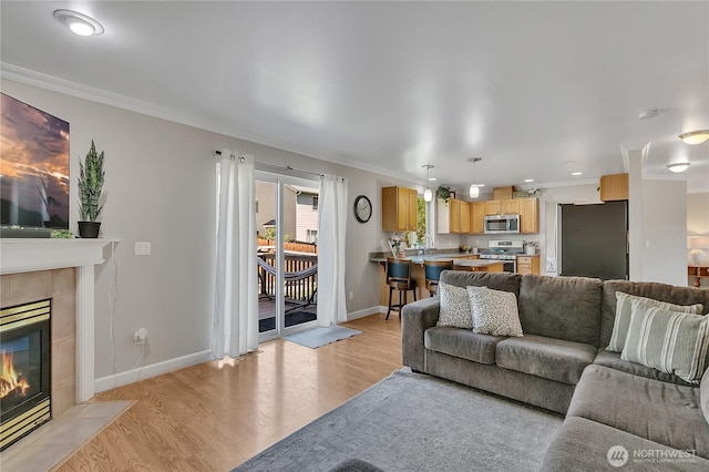 living area with ornamental molding, light wood-style floors, a tile fireplace, and baseboards