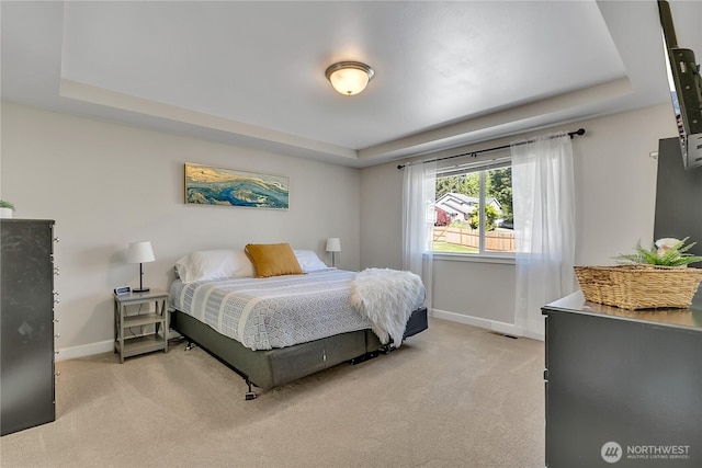 bedroom featuring a raised ceiling, baseboards, and light carpet