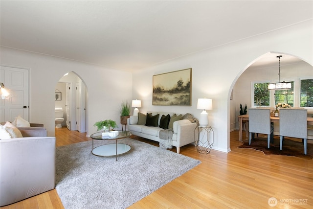 living room featuring arched walkways, baseboards, a chandelier, and light wood-style flooring